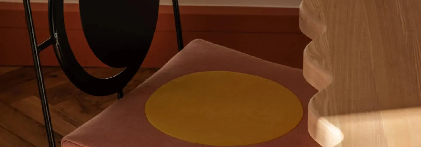 Close-up of a chair with a brown cushion featuring a large yellow circle and a wooden table with a carved edge nearby.