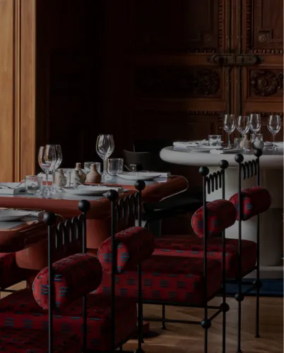 Elegant restaurant interior with round and rectangular tables set with wine glasses and red cushioned chairs.