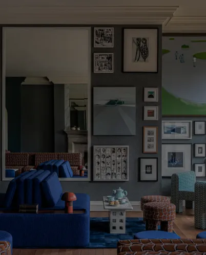 Modern living room with blue couches, a coffee table set with a tea set, assorted framed art on the gray wall, and patterned chairs.