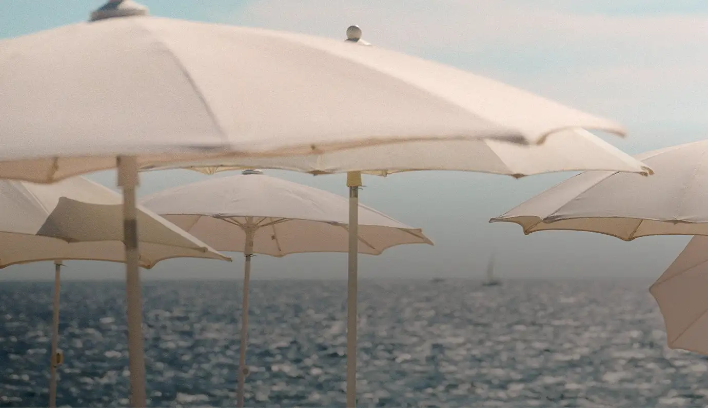 White beach umbrellas with the sea and a distant sailboat in the background under a clear sky.