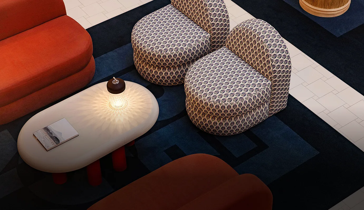 Modern living room setup with patterned armless chairs, a white oval coffee table with a decorative lit lamp, a book, and burnt orange sofas on a dark blue geometric rug.