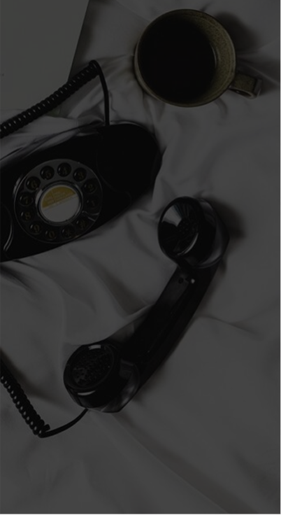 Black vintage rotary dial telephone with handset off the cradle on white fabric next to a ceramic cup.