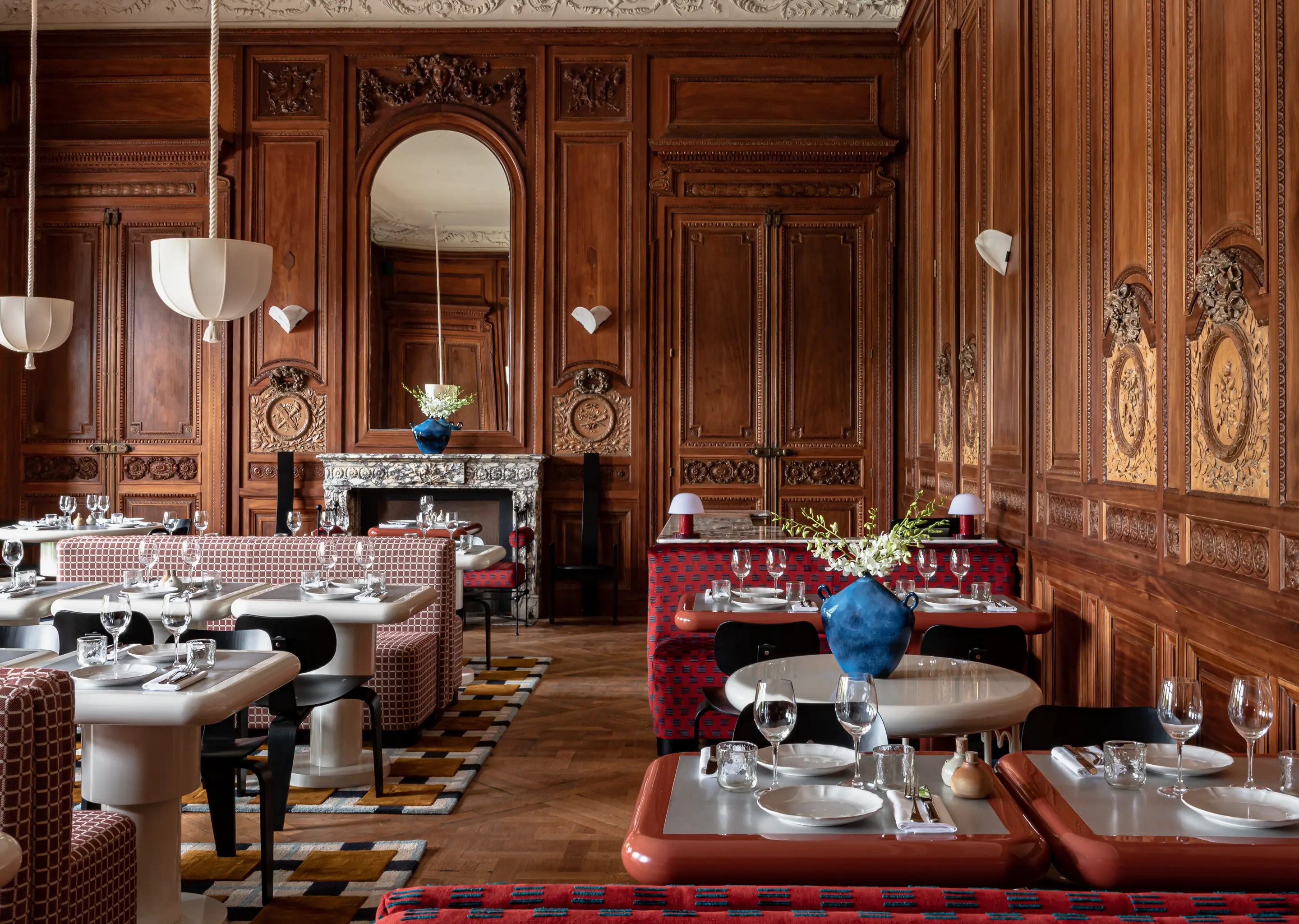 Elegant restaurant interior with ornate wooden panels, marble fireplace, patterned seating, and tables set with glassware and white plates.