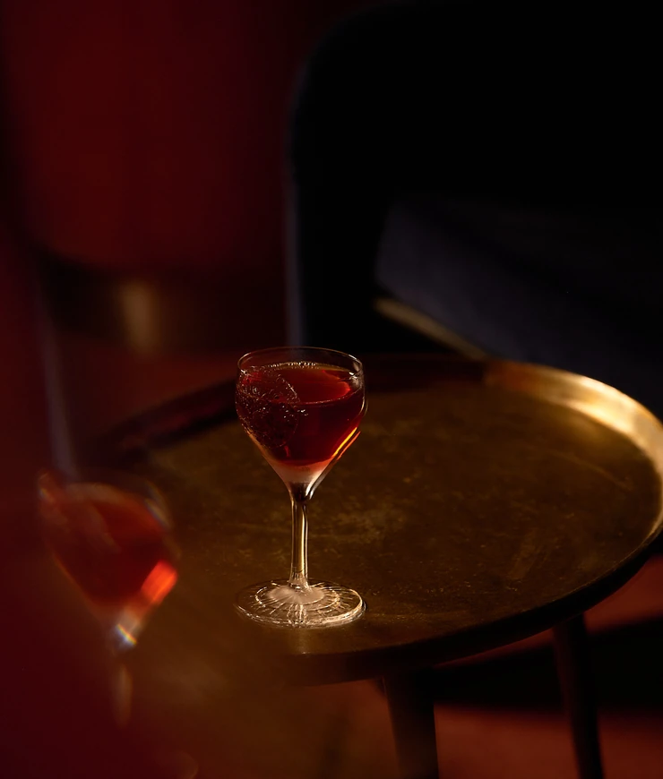Cocktail glass with a dark red drink on a round brass table in low light.