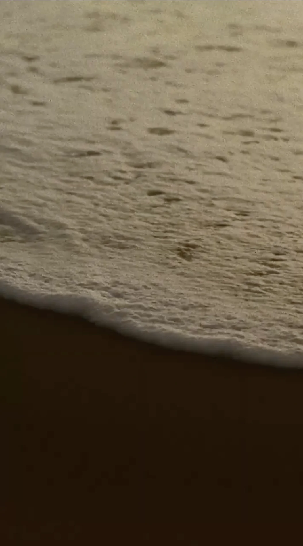 Ocean wave gently rolling onto a sandy beach at sunset.