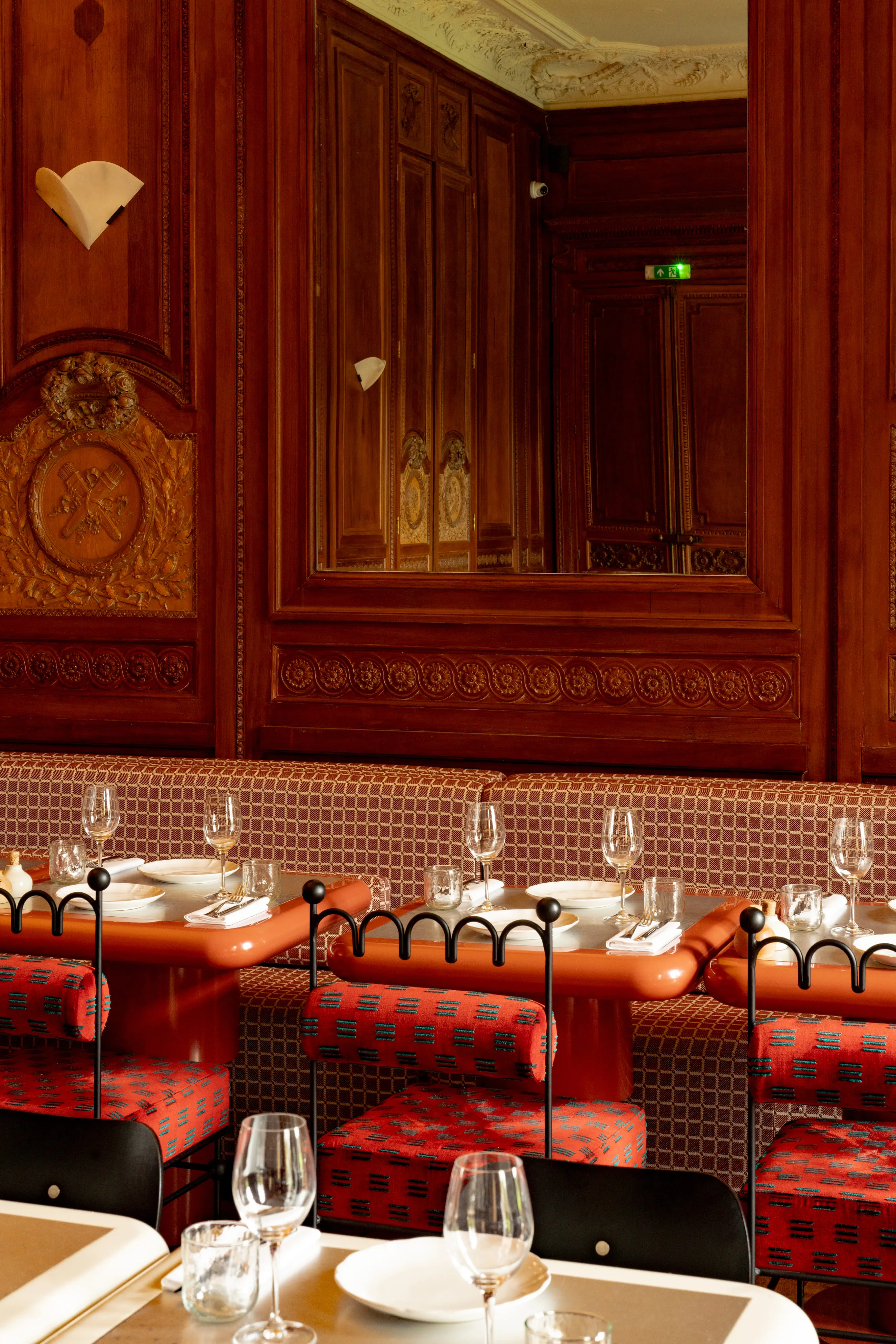 Elegant restaurant interior with wood-paneled walls, a large mirror, and tables set with wine glasses and plates.