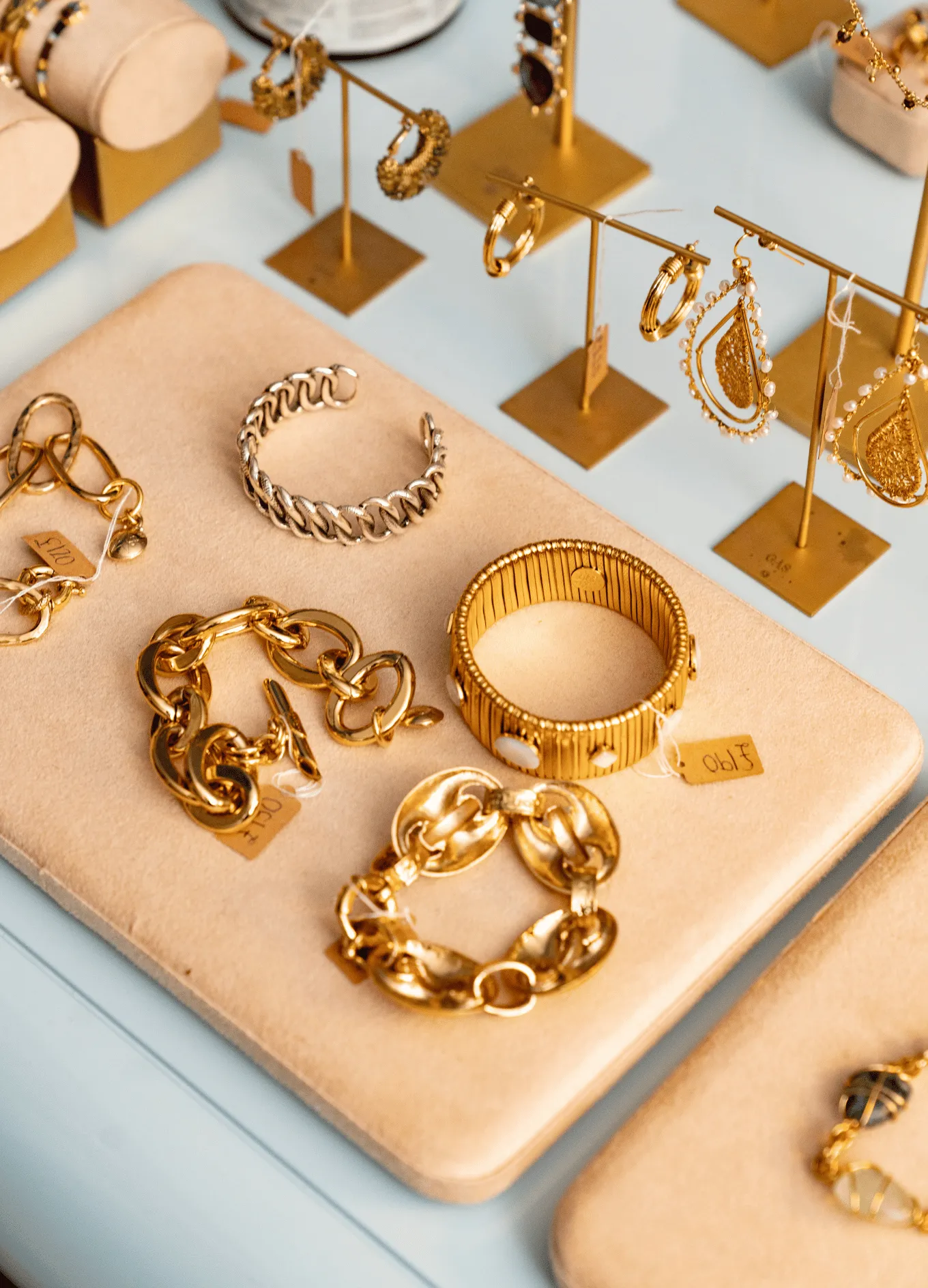 Display of gold and silver bracelets and gold earrings on beige pads in a jewelry store.