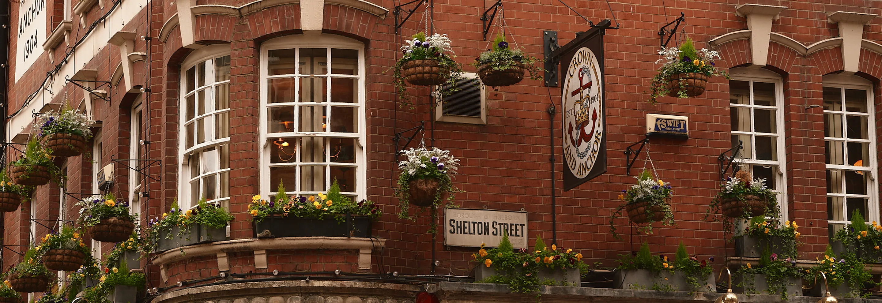 Red brick building on Shelton Street with multiple white-framed windows adorned with hanging flower baskets and window boxes.