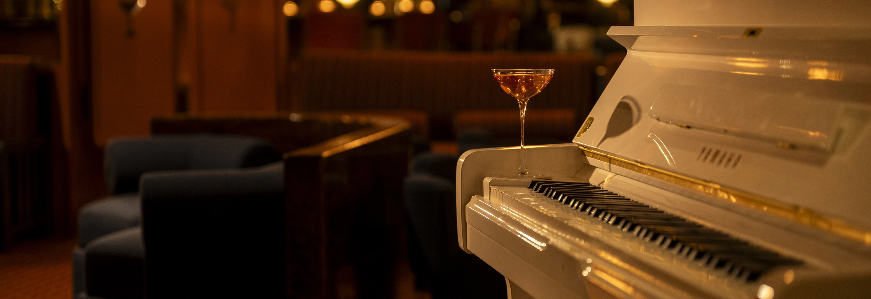 White piano with a cocktail glass placed on its edge in a cozy dimly lit lounge setting.