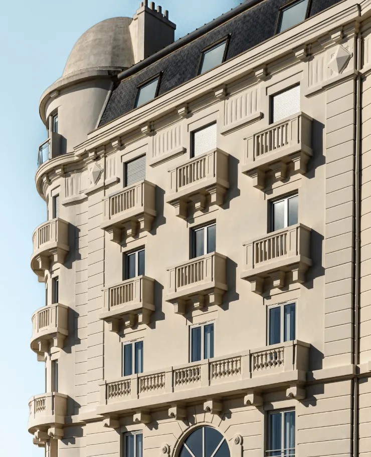 Facade of an elegant beige building with multiple decorative balconies and a rounded tower corner under a clear sky.