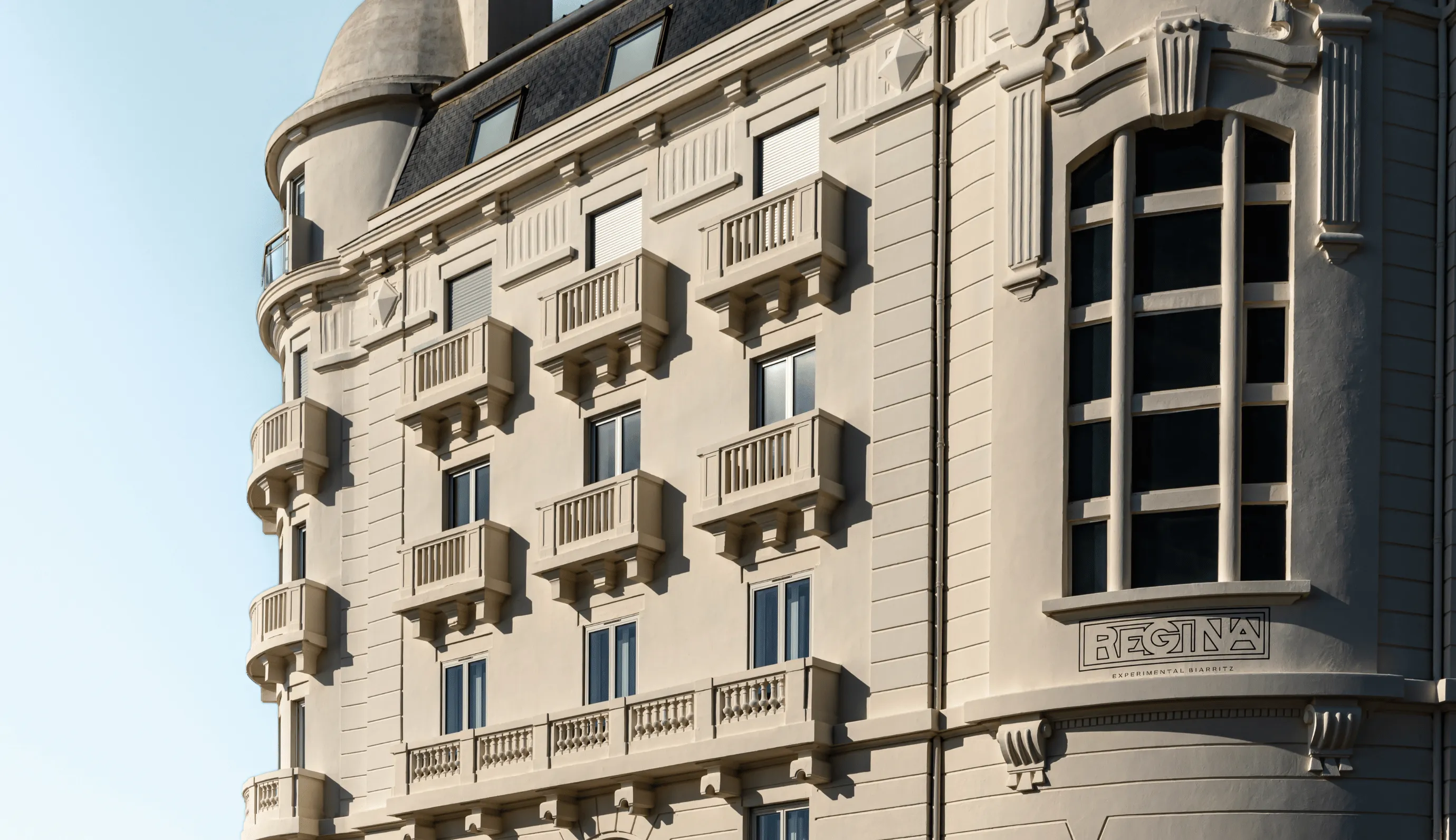 Exterior facade of Hotel Regina in Biarritz, featuring multiple small balconies and large windows under clear blue sky.