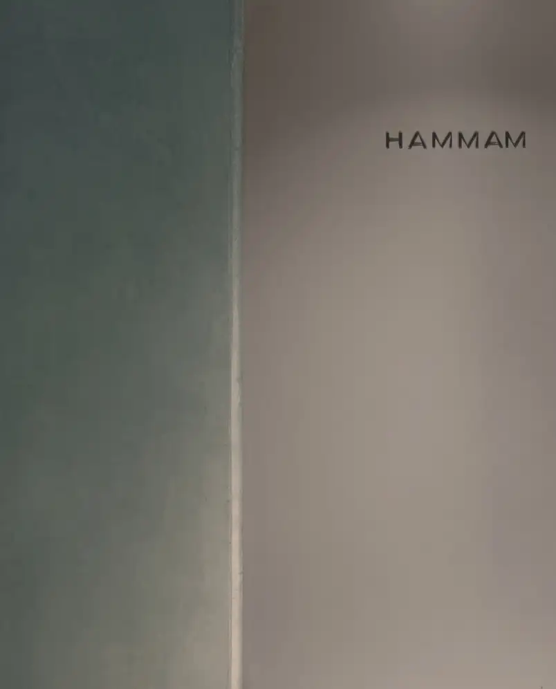 Minimalist wall section with the word 'HAMMAM' written on a plain light-colored surface next to a darker wall.