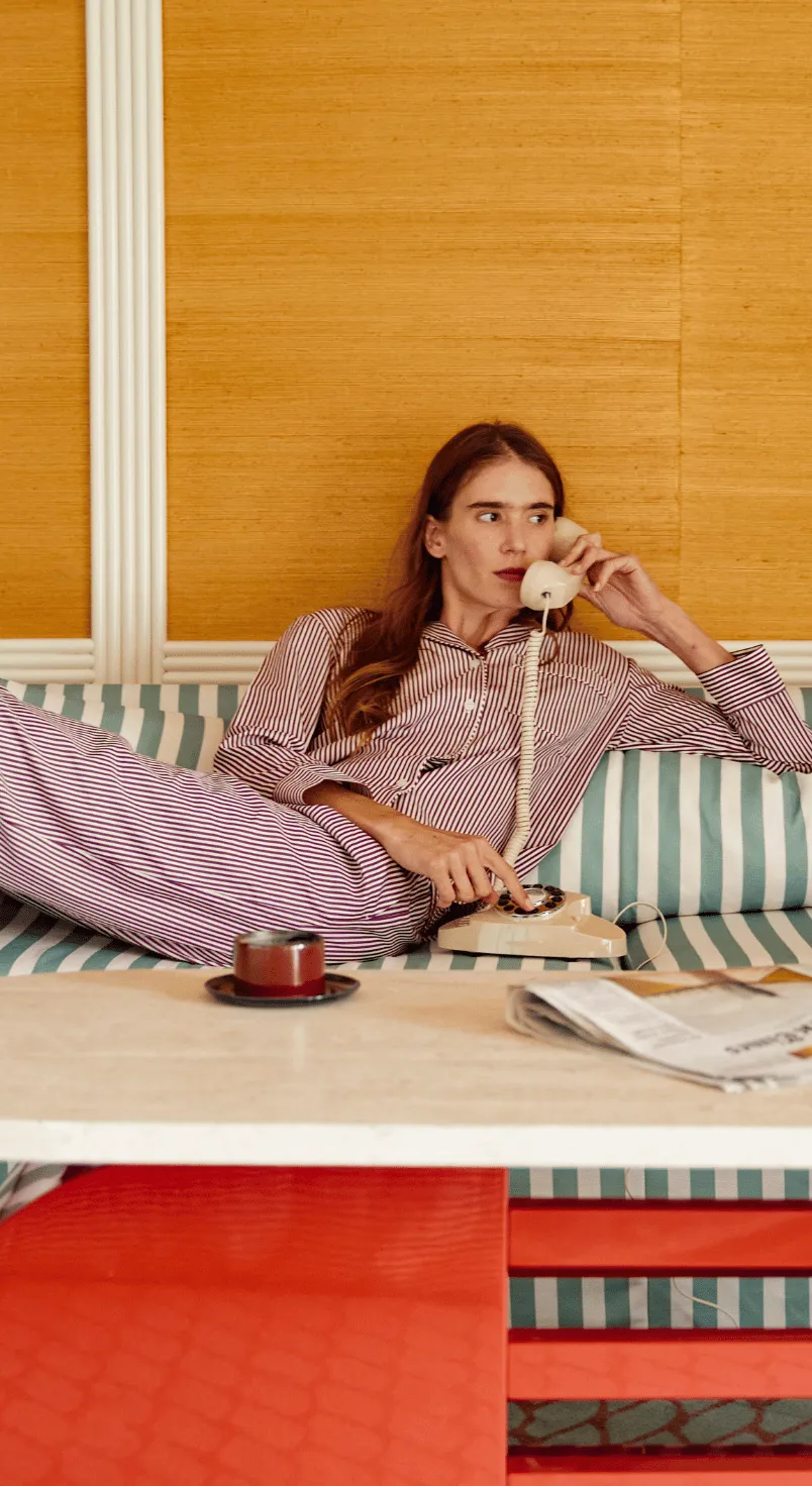 Woman wearing striped pajamas reclining on a striped couch while using a beige rotary phone.