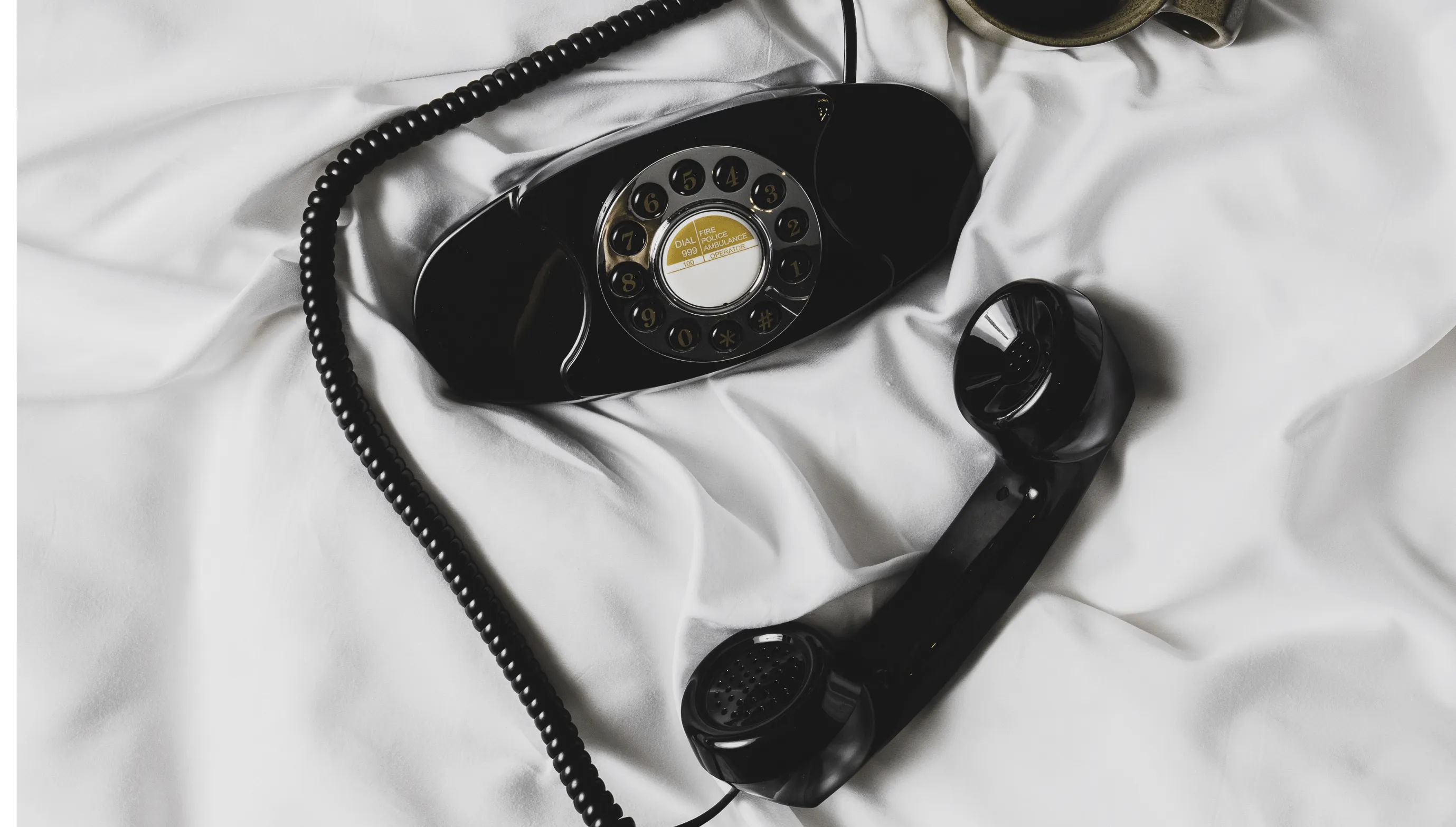 Black vintage rotary dial telephone with handset resting on white fabric.