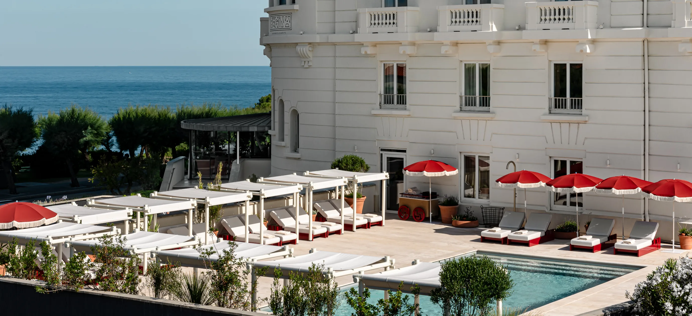 Outdoor swimming pool with sun loungers and red umbrellas in front of the Experimental Group hotel in Biarritz, Basque Coast.