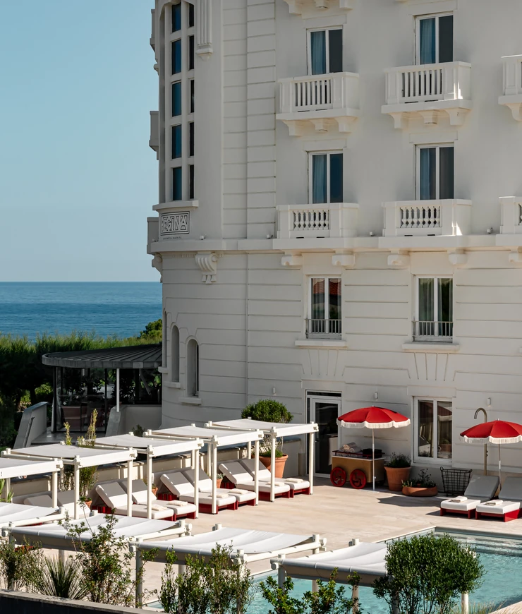 Exterior view of the historic architecture and poolside terrace at Hôtel Régina Experimental, overlooking the ocean in Biarritz.