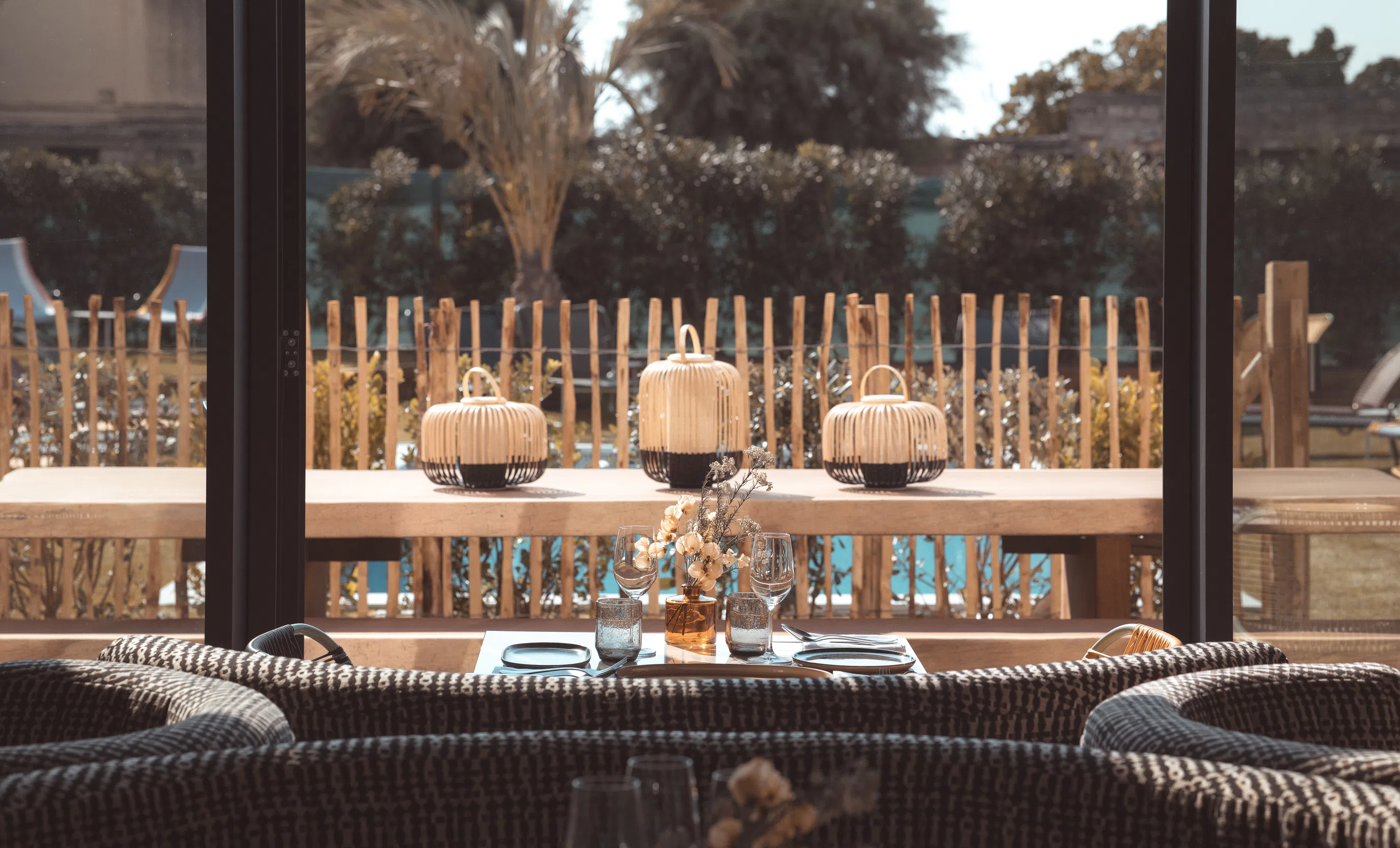 View through large glass doors from the interior lounge to the outdoor dining deck and pool at Hôtel Le Garage, Biarritz.