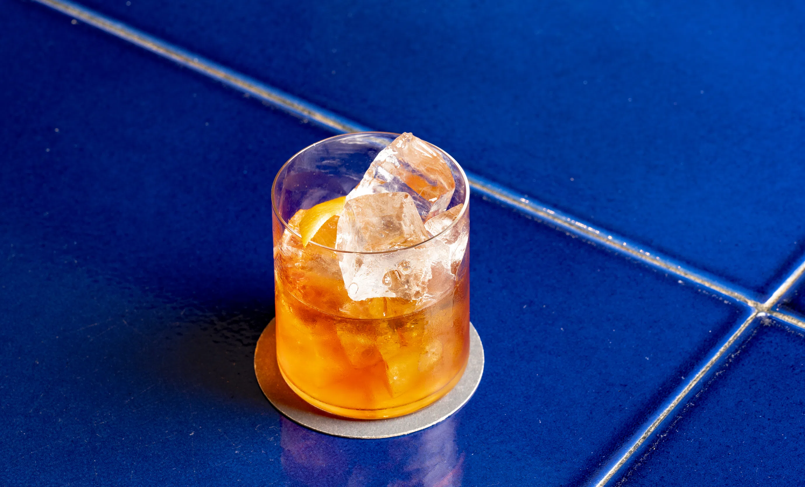 Close-up of a cocktail on ice in a tumbler glass on a blue ceramic table at Cowley Manor, Cotswolds.