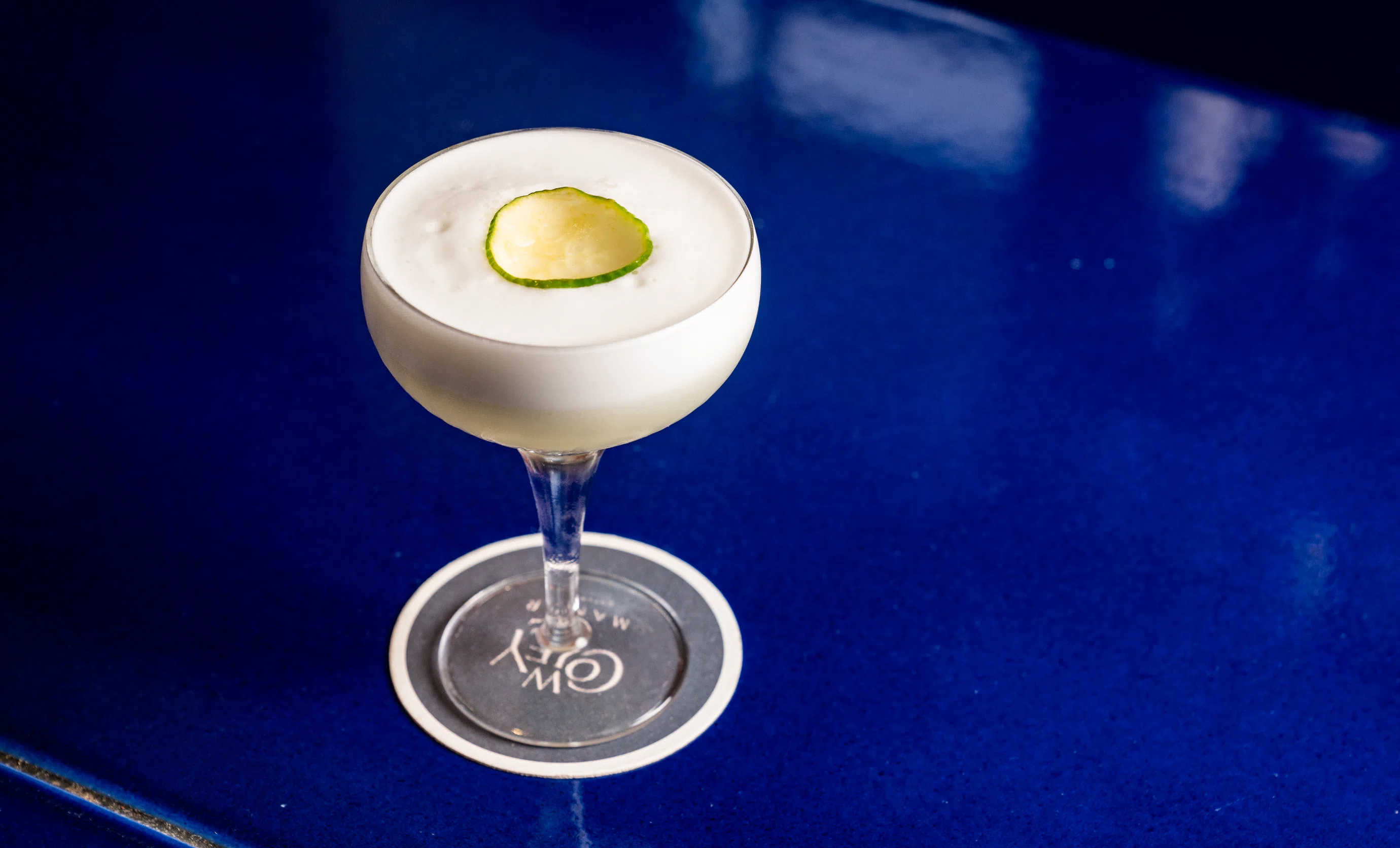 Elegant cocktail topped with a cucumber slice, served on a blue table at Cowley Manor, Cotswolds.