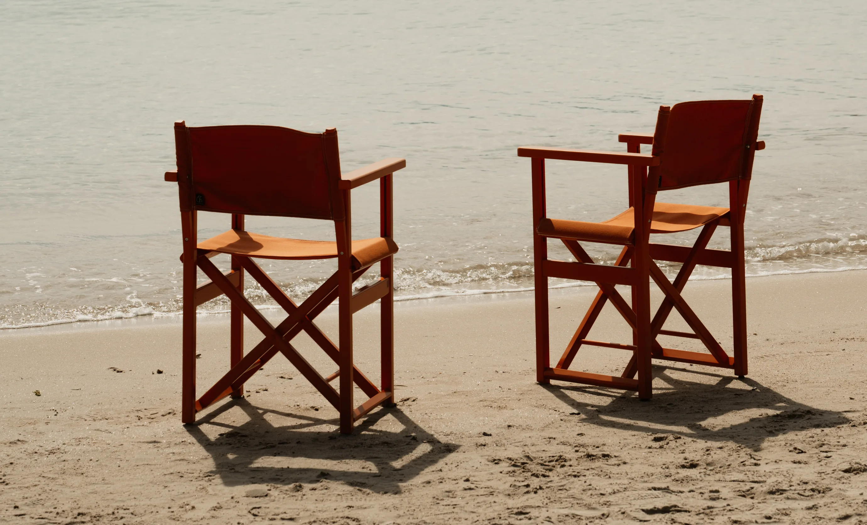 Two empty orange director's chairs placed on the sandy beach at an Experimental Group seaside location.