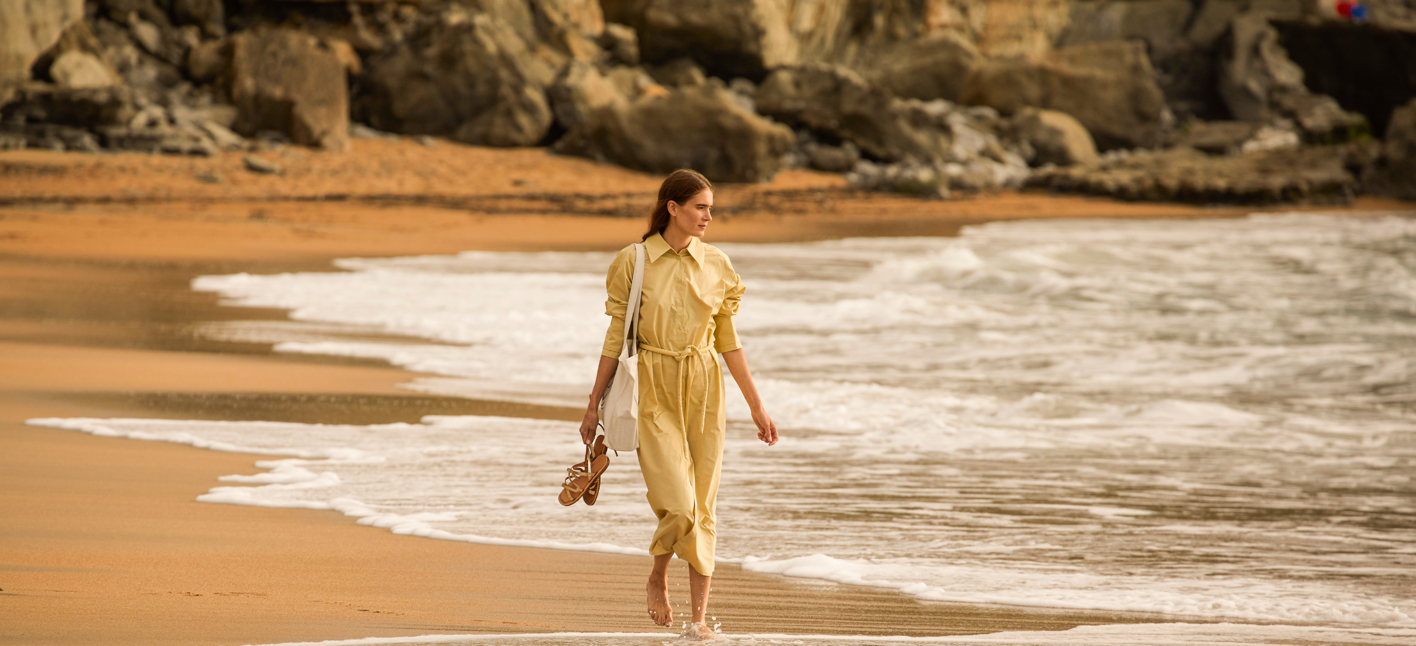 Woman walking along the sandy beach, representing the lifestyle and relaxing travel experience offered by Experimental Group destinations.