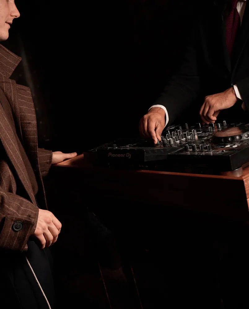 Side view of a guest in an elegant suit near a DJ console, sophisticated lifestyle atmosphere at an Experimental Group hotel.
