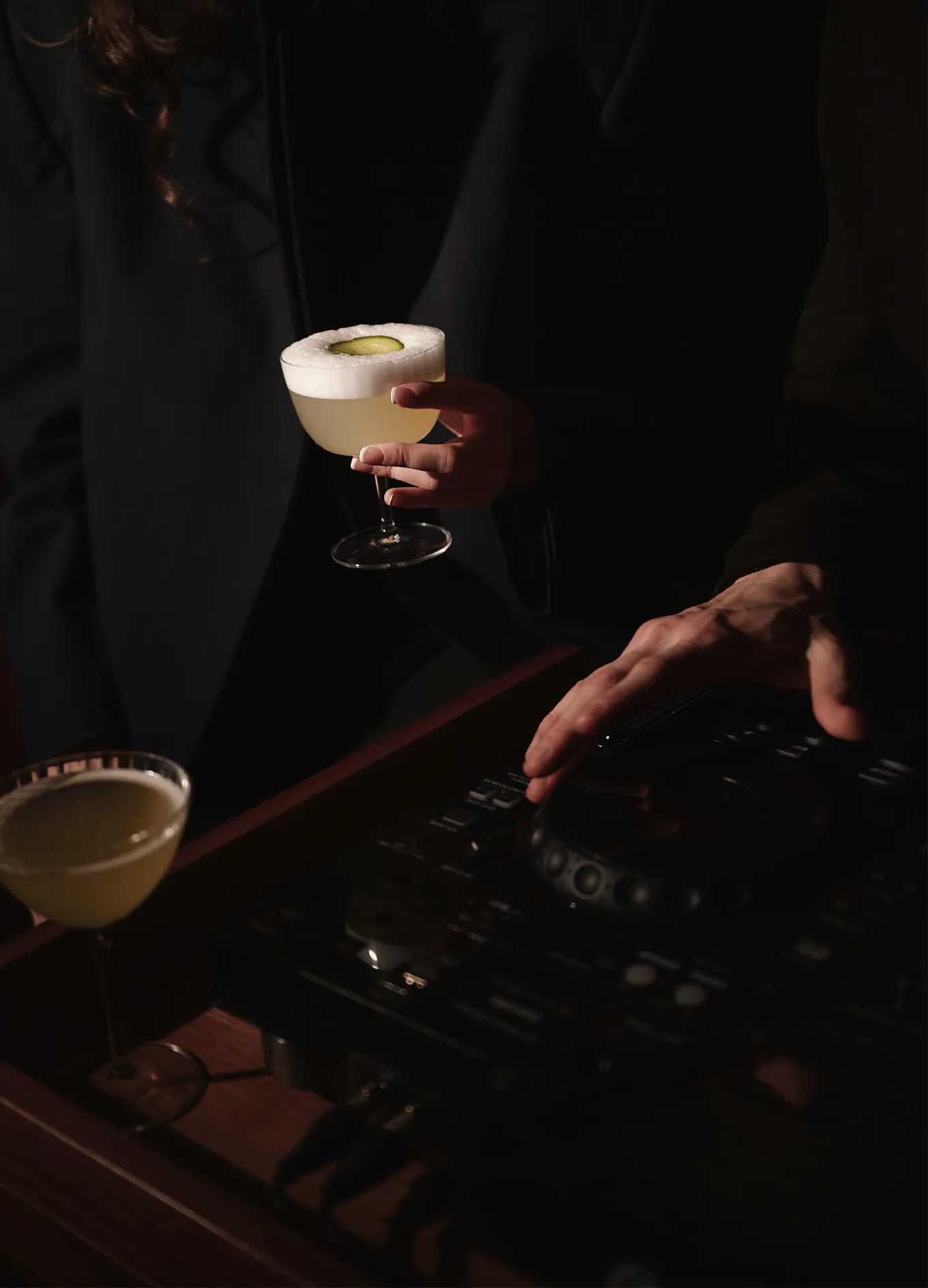 Signature cocktail garnished with a cucumber slice held by a guest at a chic Experimental Group cocktail bar.