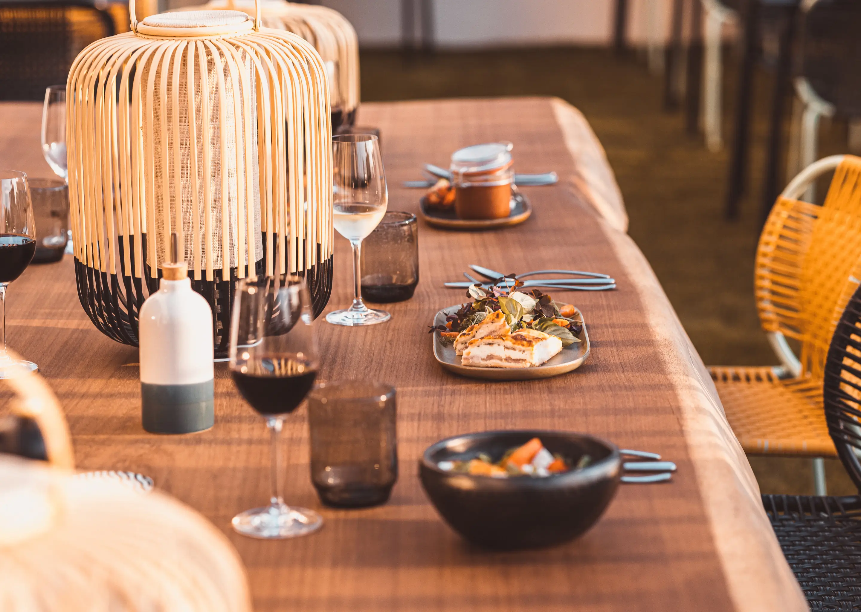 Terrace with wooden table, bamboo lanterns, elegant tableware, and rattan chairs from the Experimental Group.
