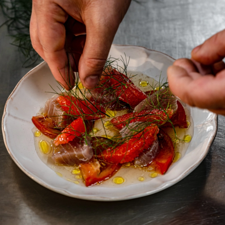Chef garnishing a fish carpaccio with fresh dill, tomatoes, and olive oil at The Henrietta Hotel restaurant.