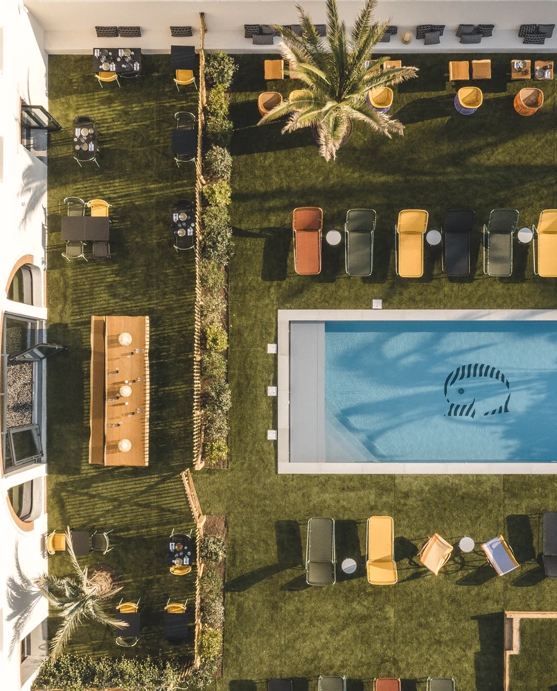 Aerial bird's-eye view of a lush green lawn, swimming pool, and lounge area at an Experimental Group hotel.