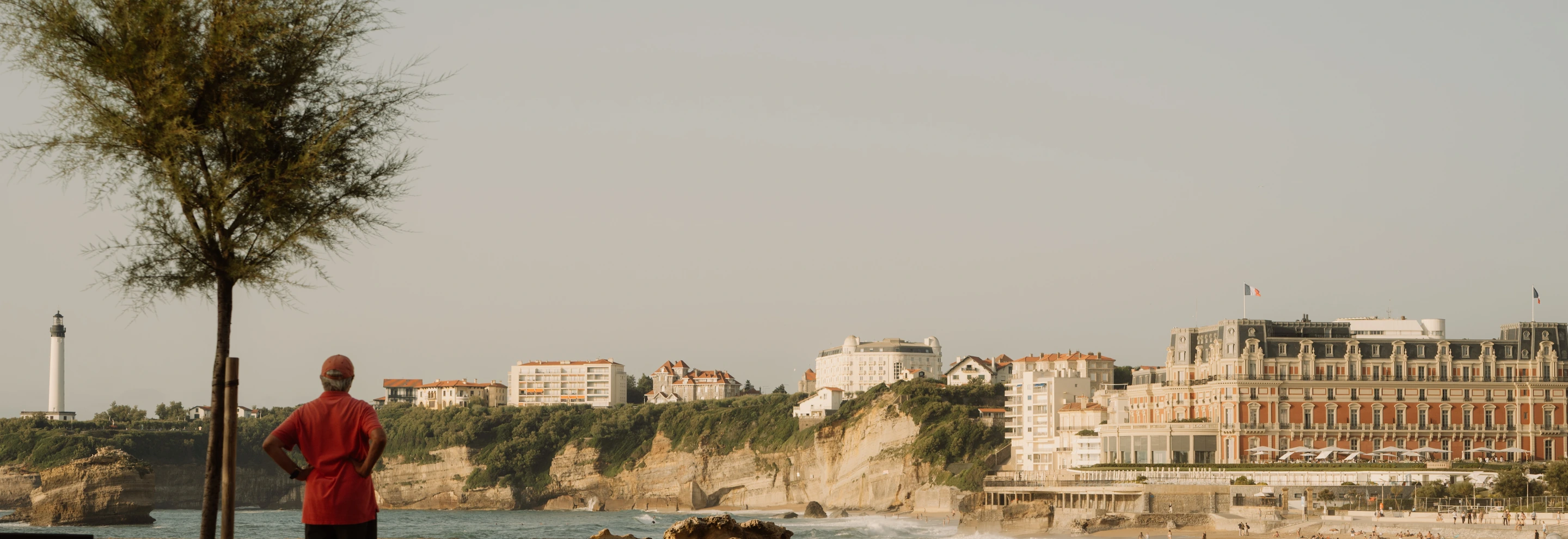 A guest gazing at the iconic Phare de Biarritz lighthouse and the historic Regina Experimental hotel building on the cliffs of the Basque coast, France.