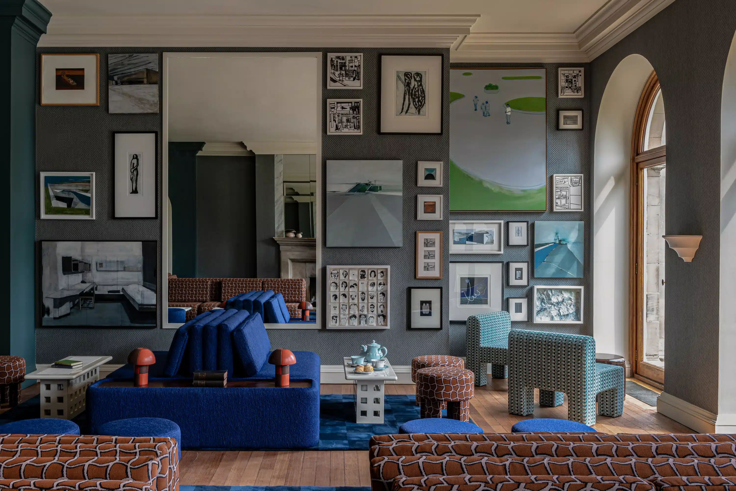 Modern living room with patterned blue and brown sofas, various framed artworks, and large window.