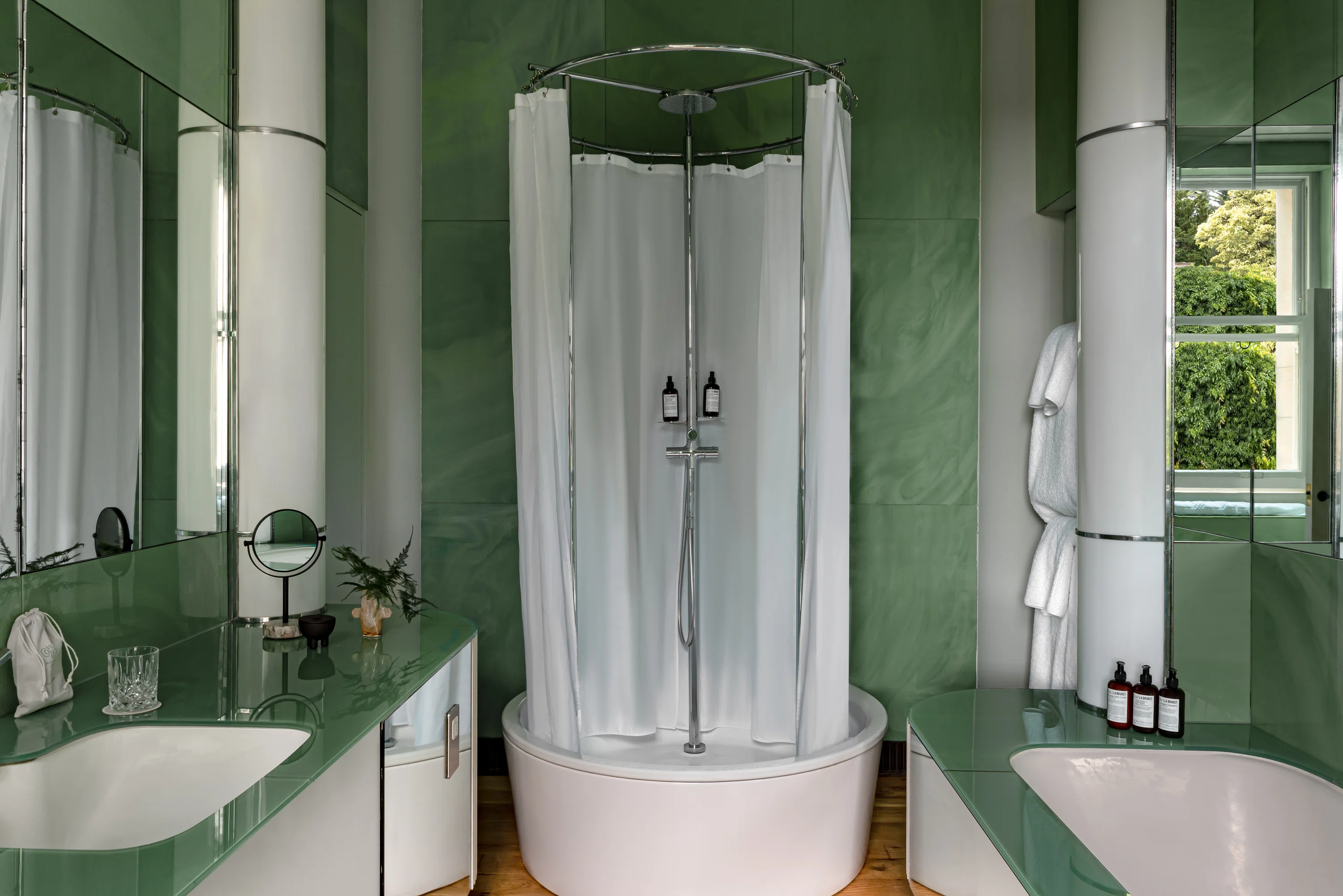 Modern bathroom with green walls, round shower with white curtain, double sinks, and mirrors.