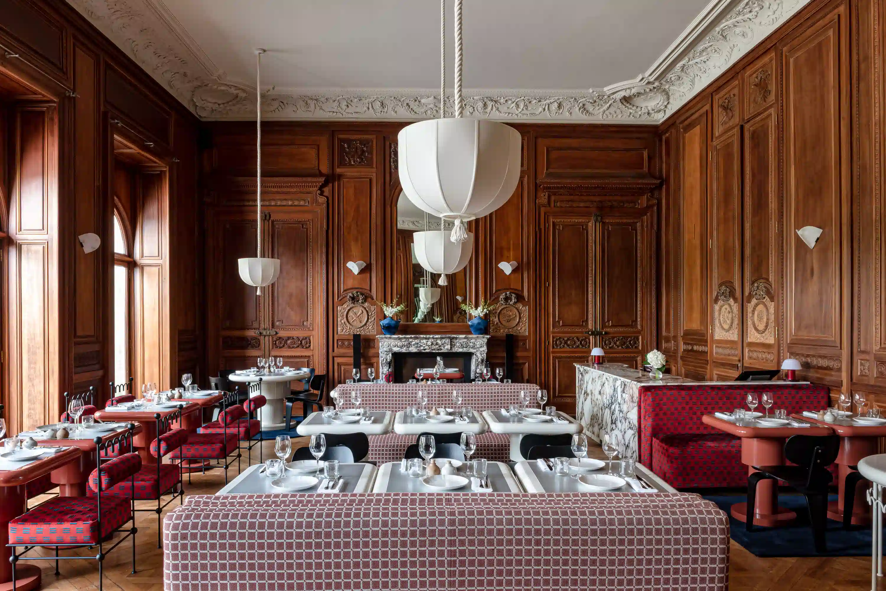 Elegant restaurant with wood-paneled walls, patterned seating, white tables, and large pendant lights.