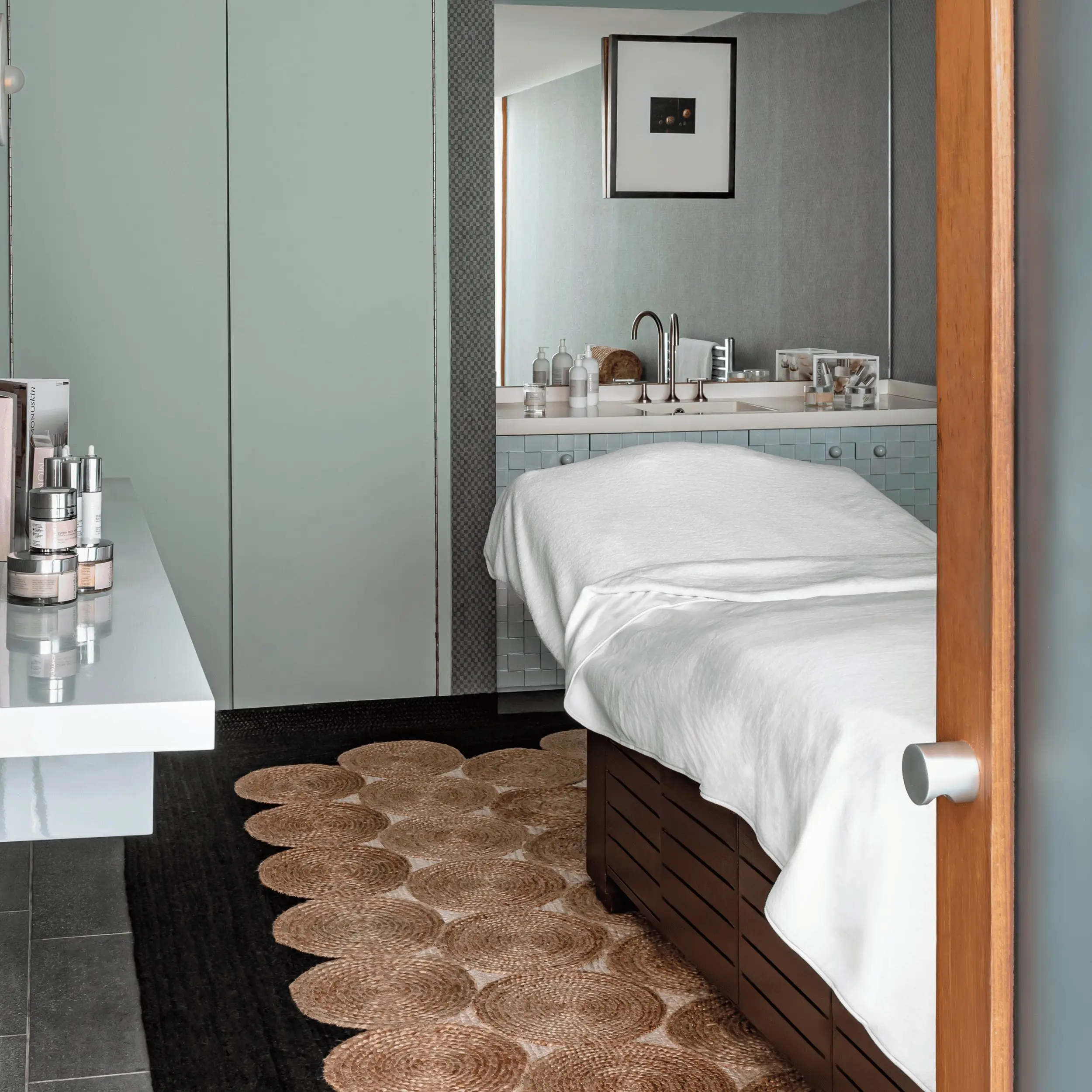 Spa room with massage table covered in white linens and skincare products on a nearby counter.