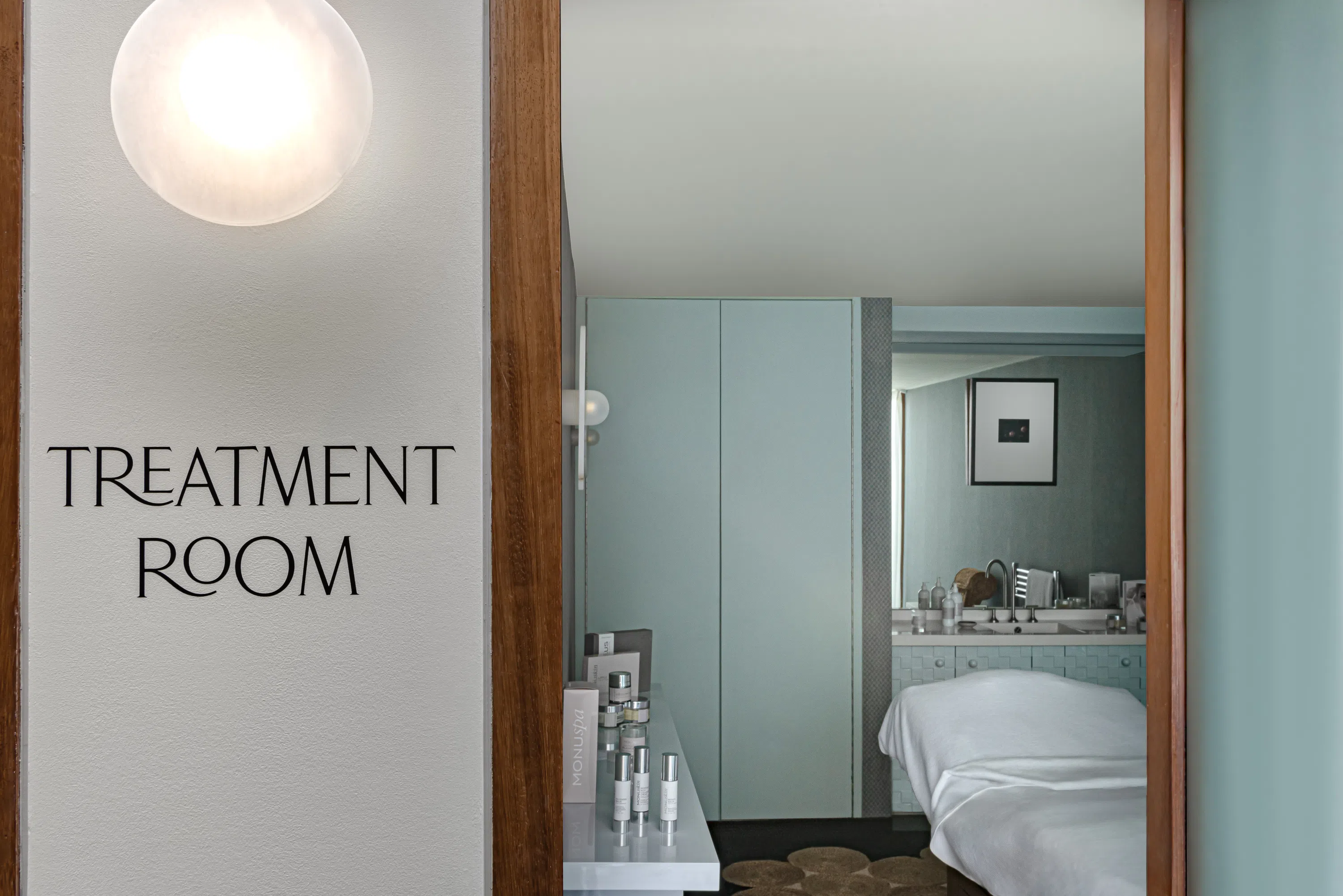 Treatment room with massage table, skincare products on a table, soft lighting, and a framed picture on the wall.