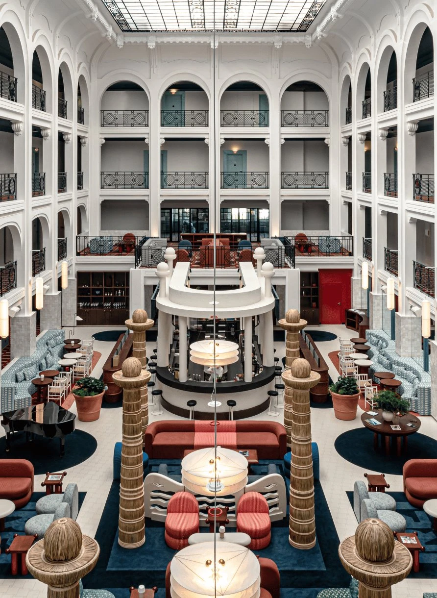 Spacious atrium with white columns, arched balconies, seating areas, and a grand piano under a glass ceiling.