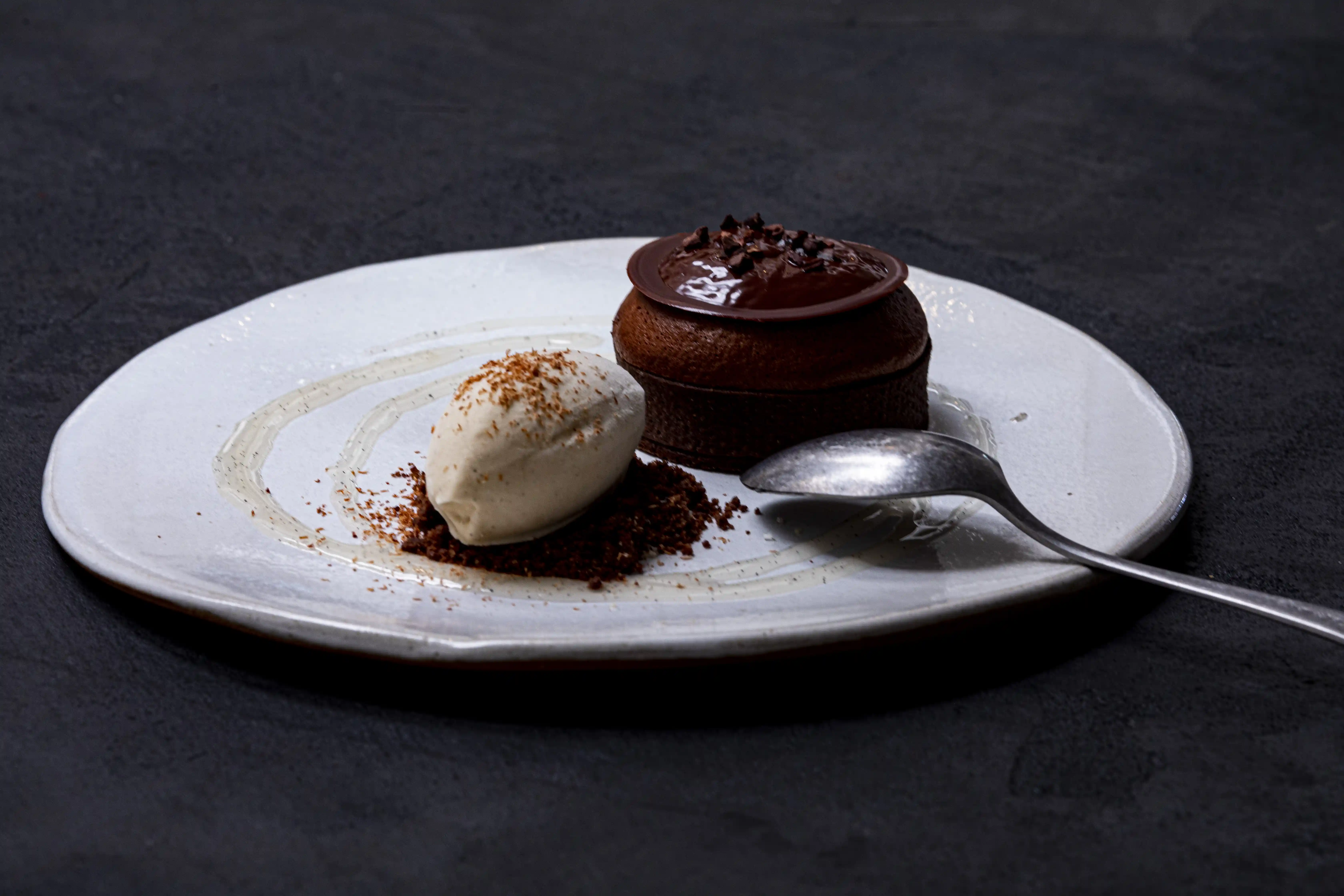 Chocolate dessert with a scoop of whipped cream and chocolate crumbs on a white plate with a spoon.