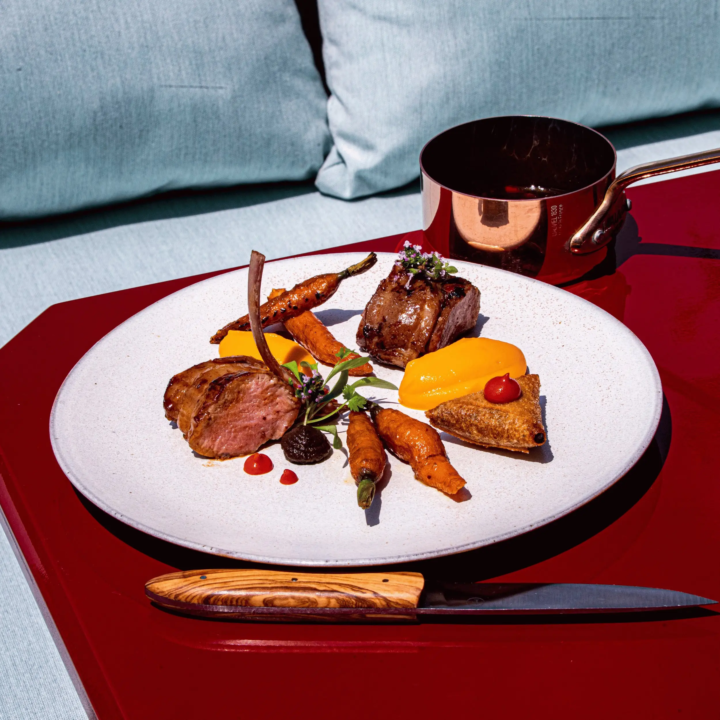 Plated gourmet meal with cooked meat, carrots, orange puree, sauce dollops, and a small pastry triangle.