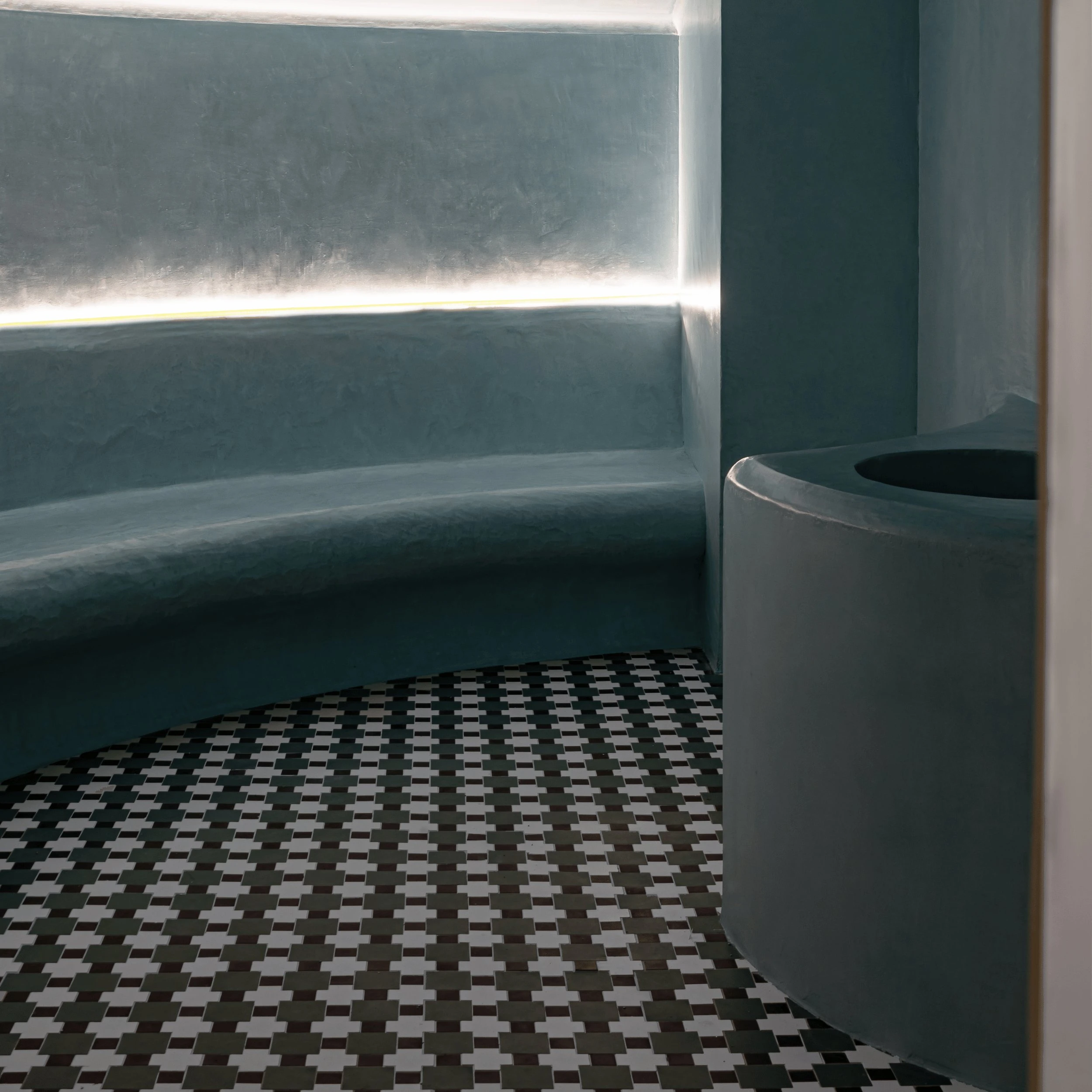 Curved gray seating with soft backlighting and black-and-white checkered floor tiles in a modern room.