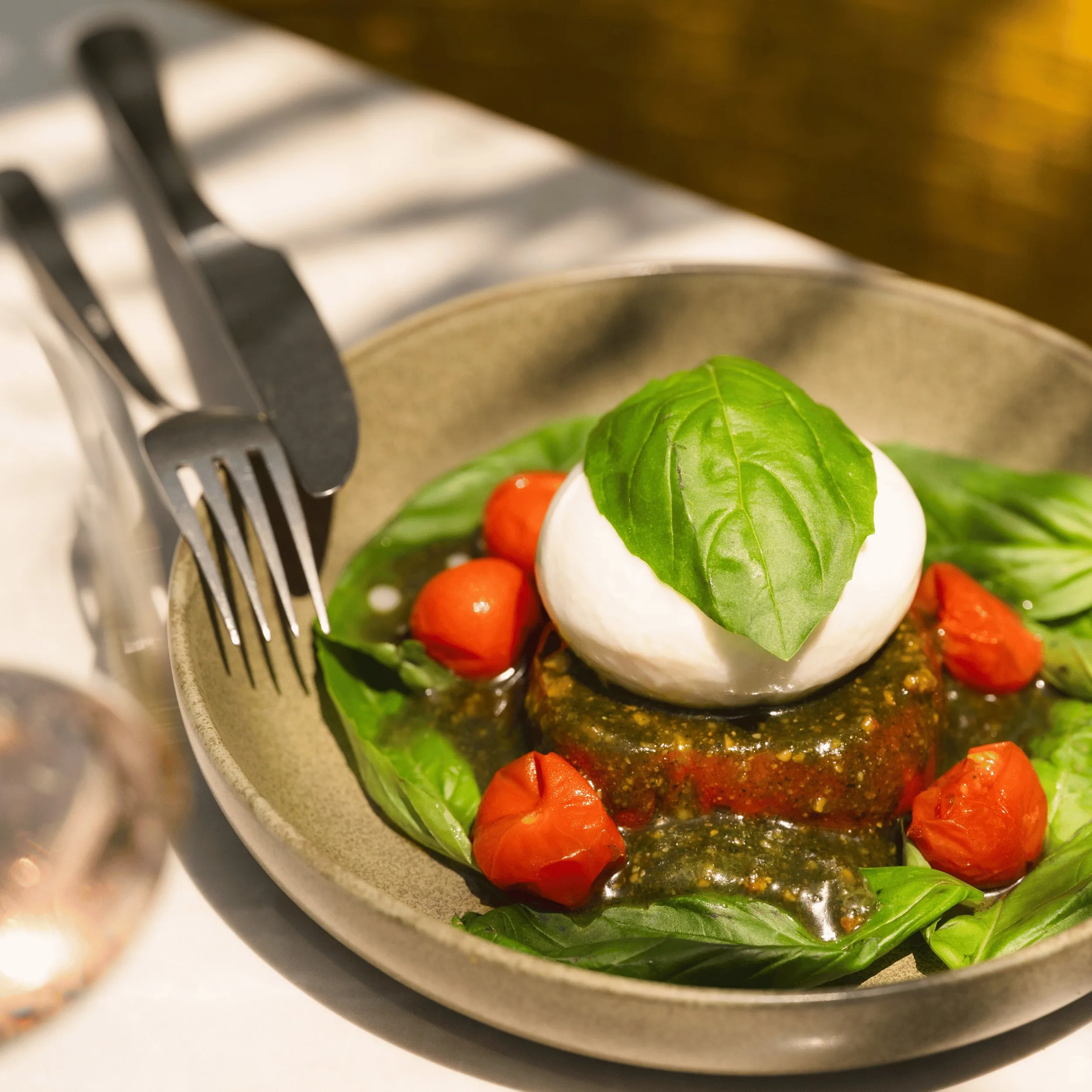 Dish with burrata cheese, fresh basil leaves, cherry tomatoes, and pesto sauce in a bowl.
