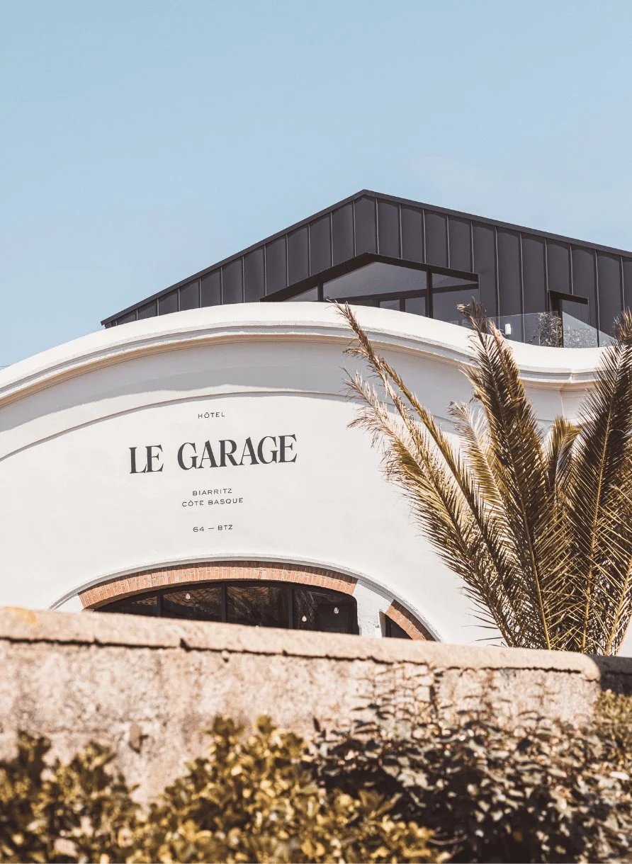 Exterior of Hôtel Le Garage in Biarritz with palm trees and modern rooftop structure.
