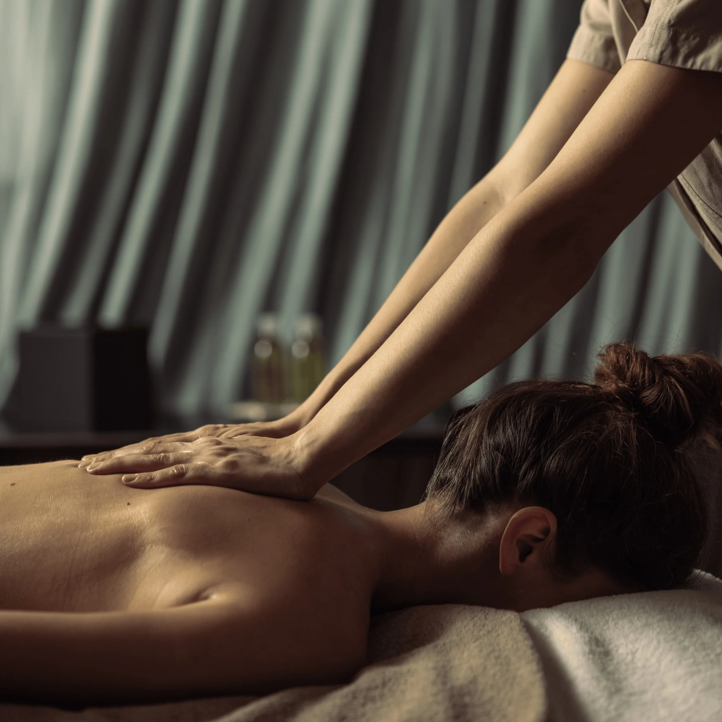Person receiving back massage with therapist's hands pressing on upper back in spa setting.