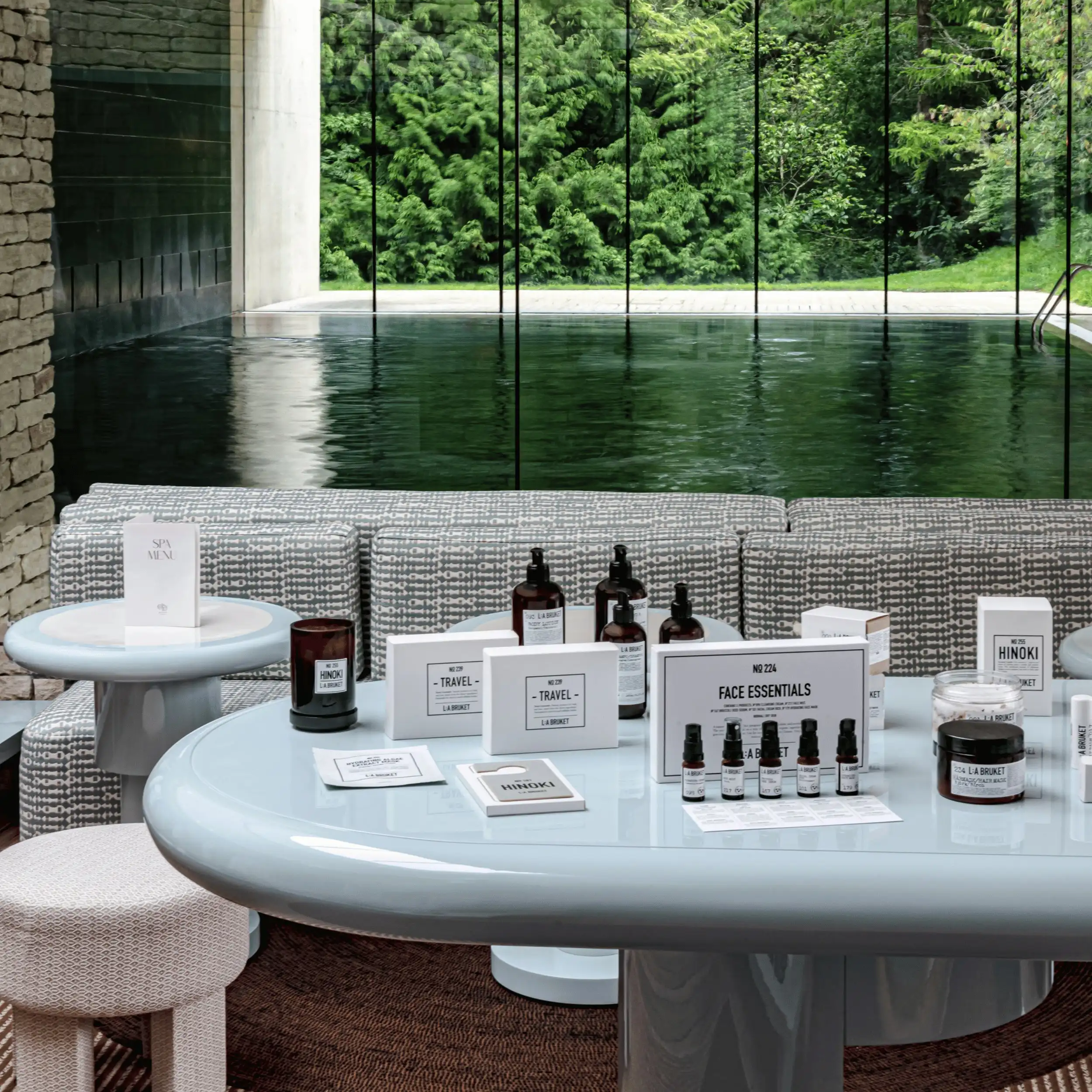 Spa wellness products displayed on a modern table with a pool and green trees visible through glass.