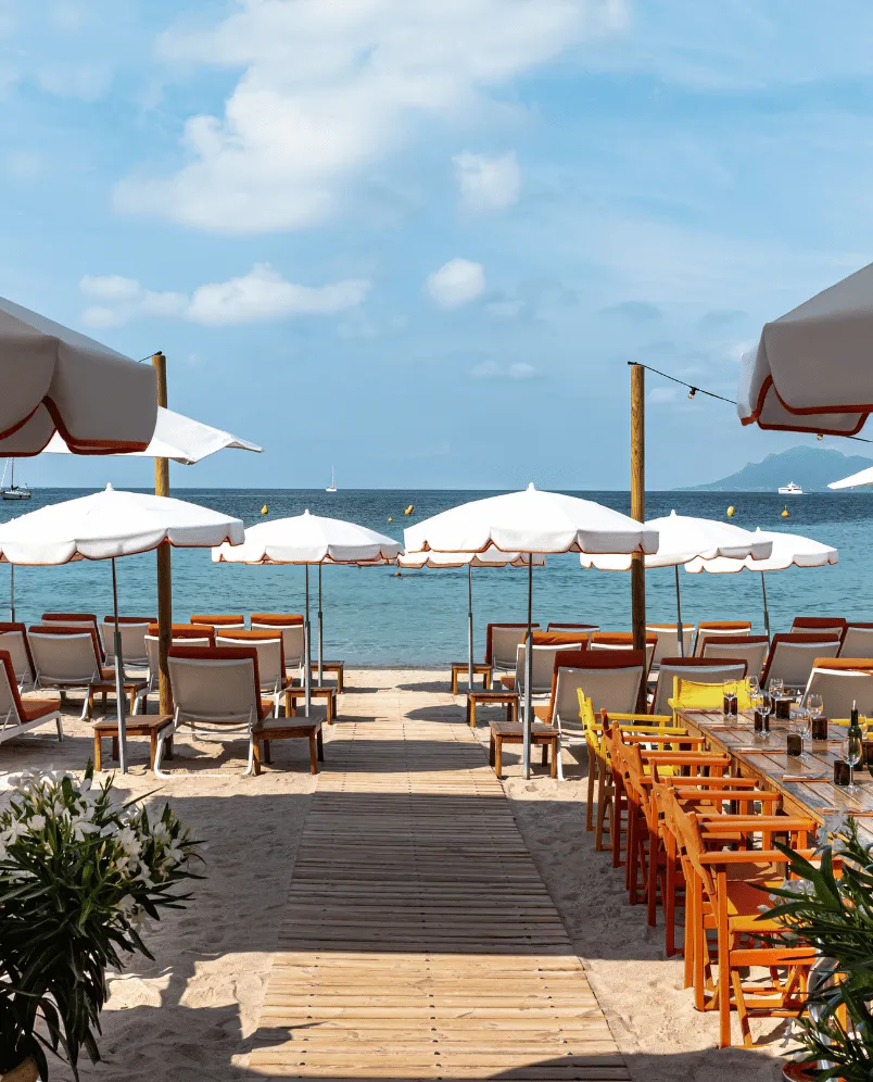 Beachfront with white umbrellas, lounge chairs, and an outdoor dining area by the sea.