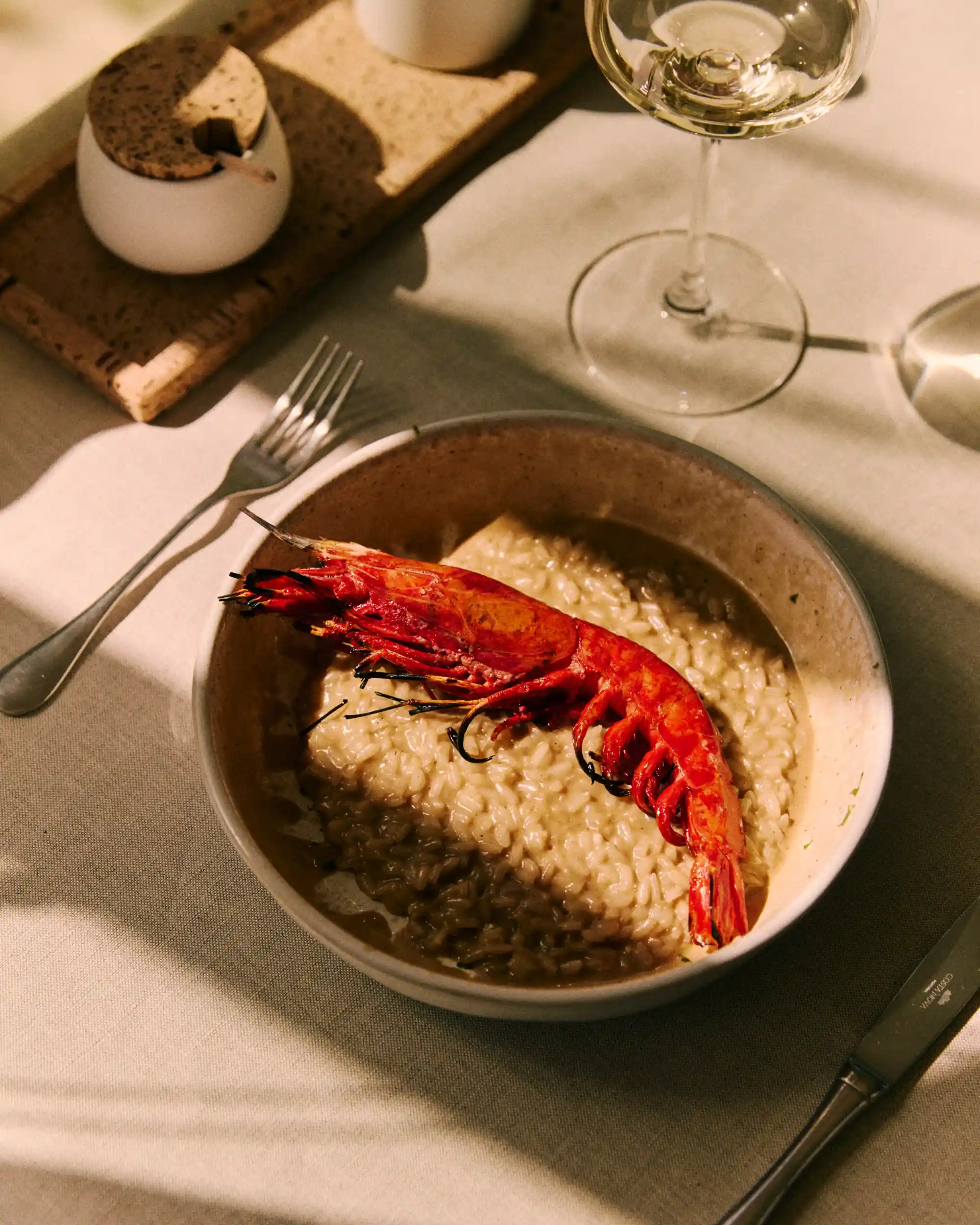 Bowl of creamy risotto topped with a large cooked red prawn on a white tablecloth.