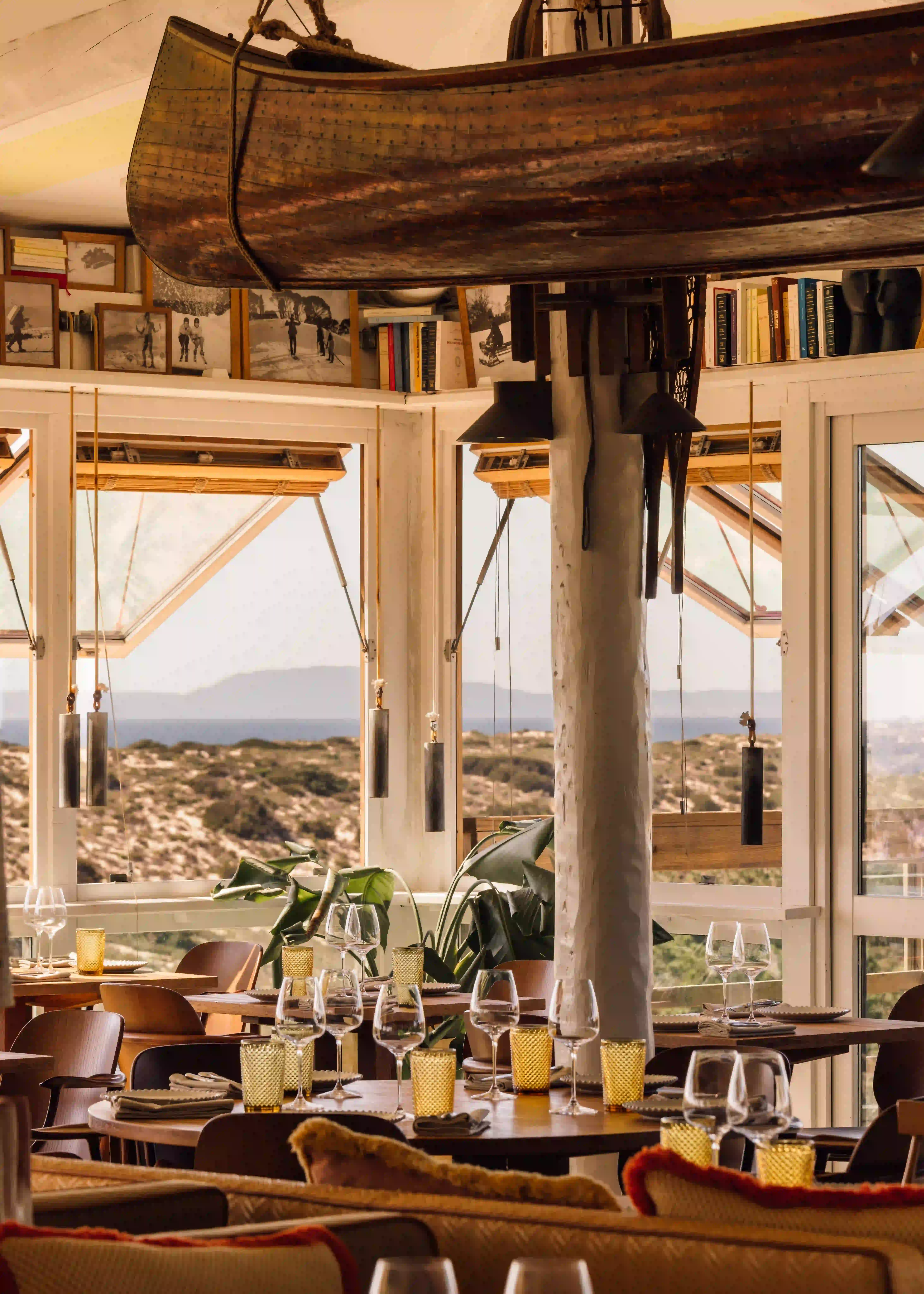 Cozy restaurant interior with wooden tables, wine glasses, yellow candle holders, and a scenic hillside view.