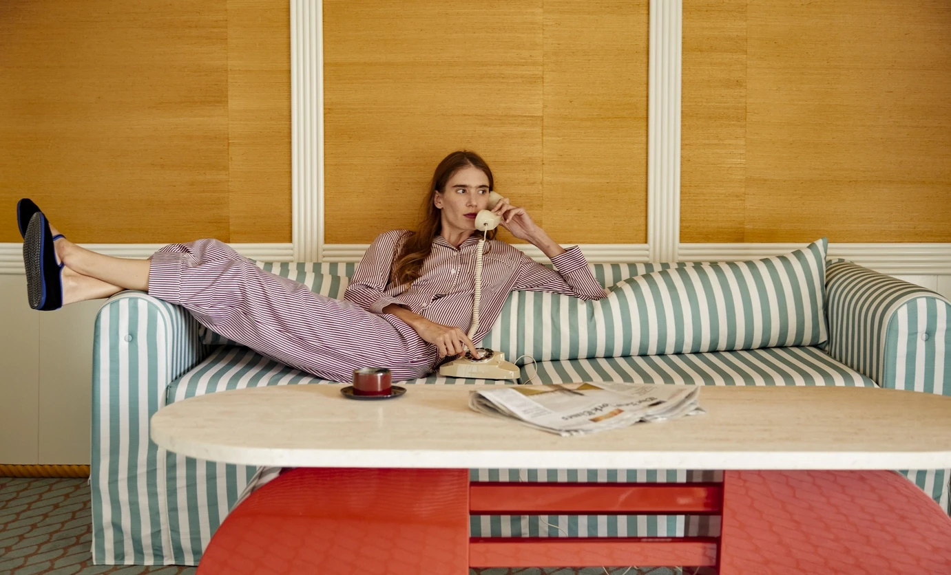 Woman in striped pajamas reclining on striped couch, holding a vintage rotary phone.