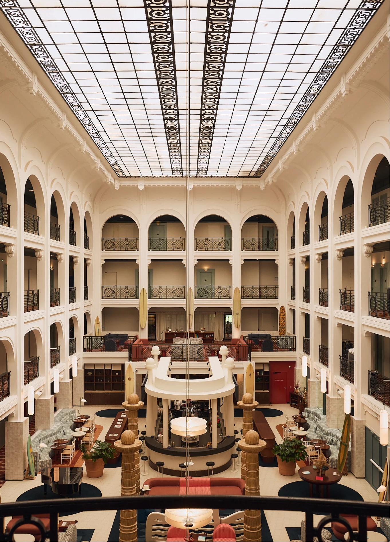 Grand indoor hotel atrium, bathed in natural light from a glass roof, with arched levels and a central reception area.