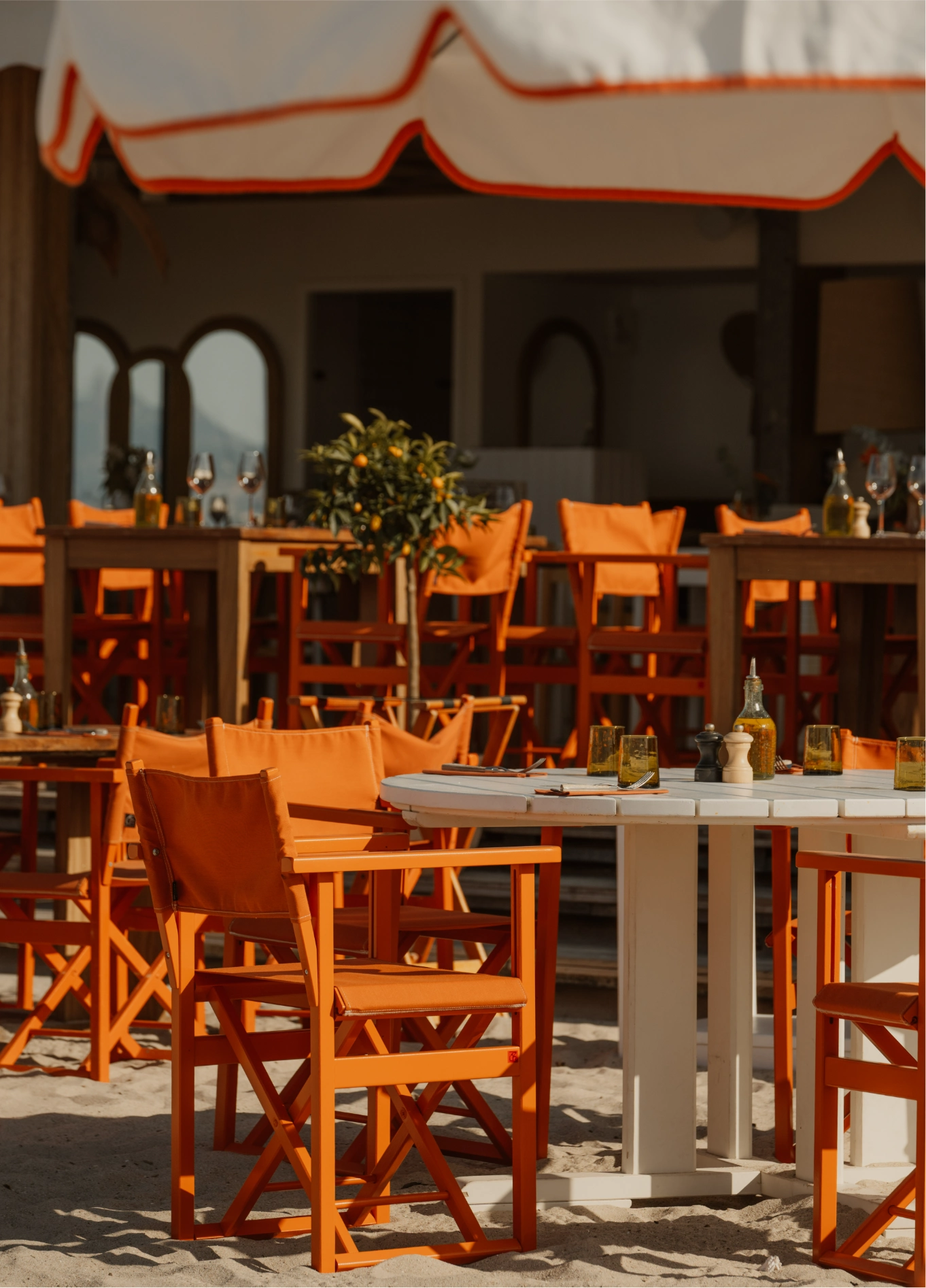 Warm and friendly outdoor dining area under a pergola, featuring wooden furniture and director-style chairs, by the Experimental Group.